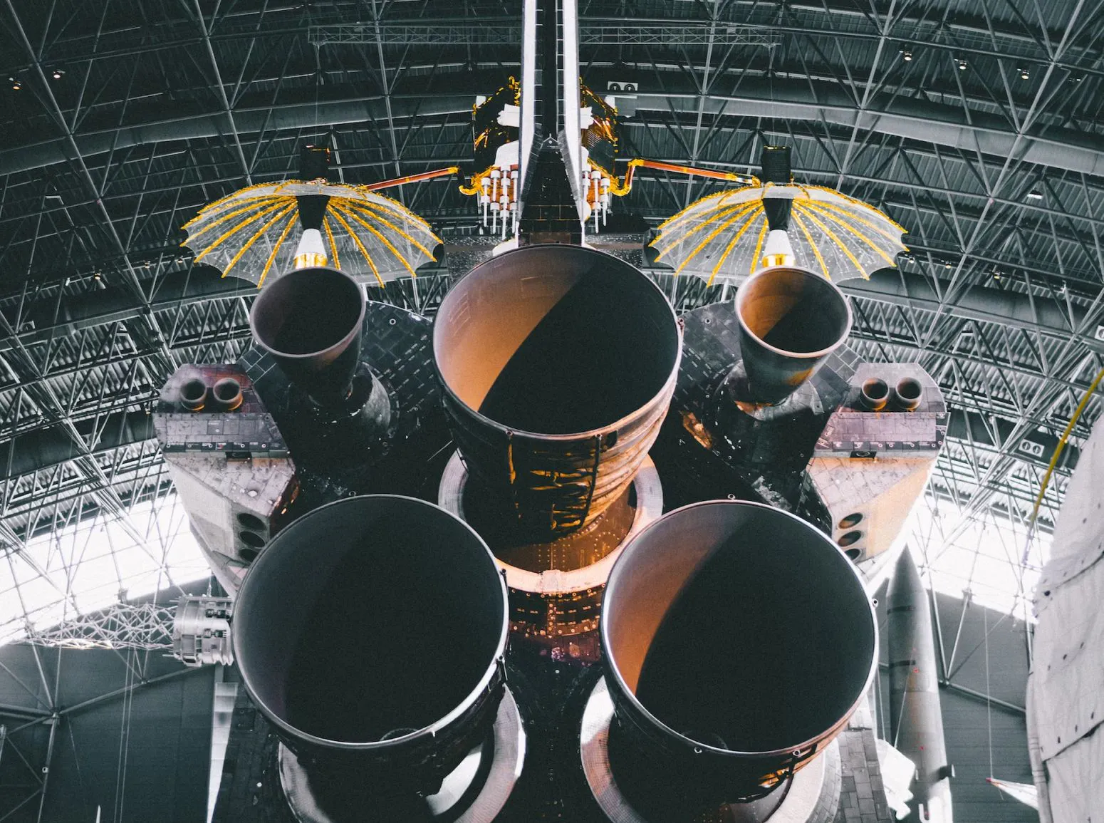 A large space shuttle featuring four prominent pipes positioned on its top surface, set against a clear sky backdrop.
